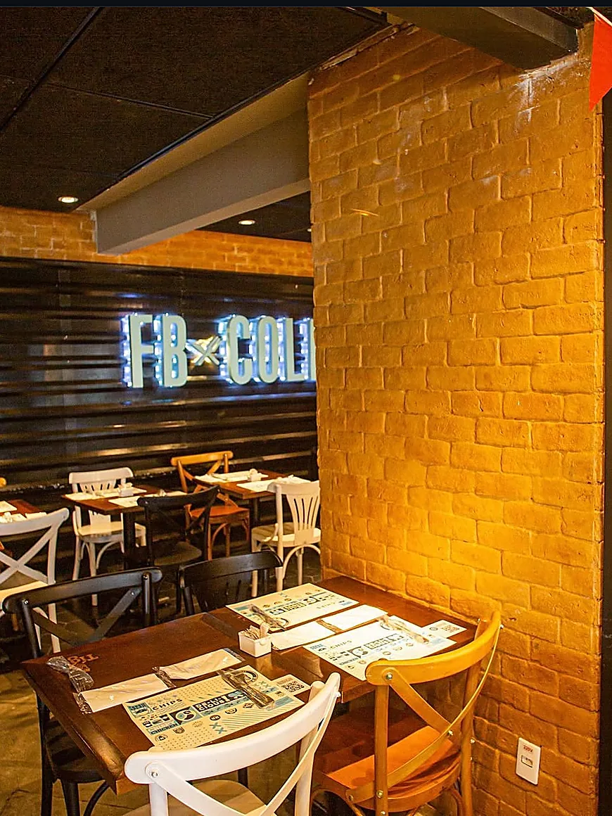 Salão de bar com tijolo aparente e letreiro em neon